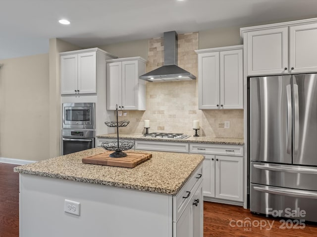 kitchen with wall chimney exhaust hood, white cabinets, dark wood-type flooring, and appliances with stainless steel finishes