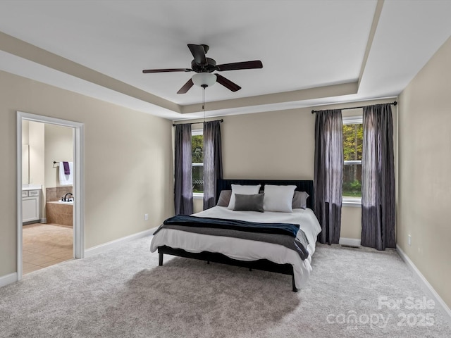 carpeted bedroom with ensuite bathroom, a raised ceiling, and ceiling fan