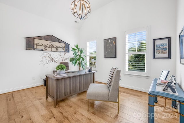 office area with light wood-type flooring, high vaulted ceiling, and an inviting chandelier