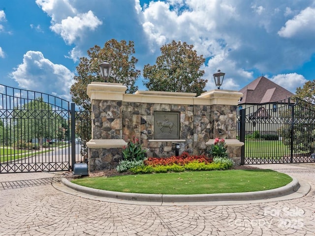 community / neighborhood sign featuring a gate, fence, and a yard