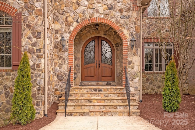 view of exterior entry featuring stone siding, brick siding, and french doors