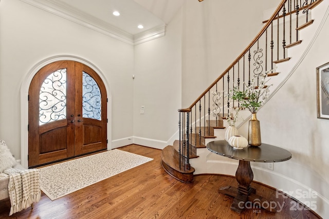 foyer featuring arched walkways, french doors, wood finished floors, and crown molding