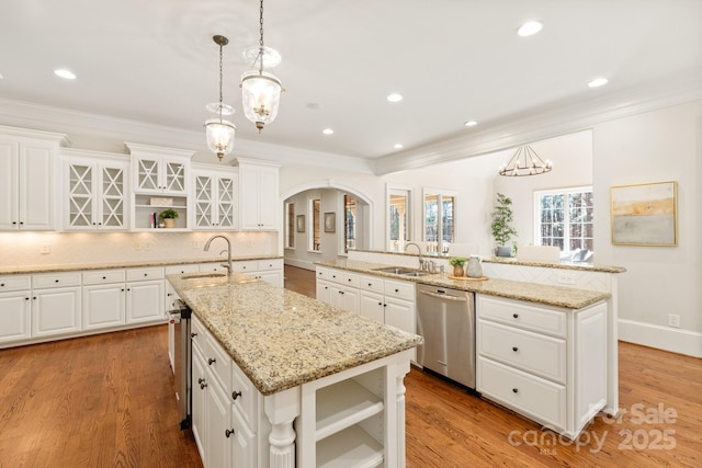 kitchen with arched walkways, a sink, dishwasher, open shelves, and an island with sink