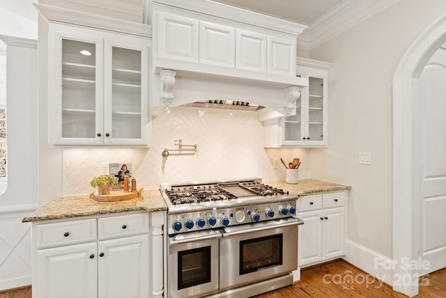 kitchen featuring range with two ovens, arched walkways, backsplash, light wood-style floors, and ornamental molding