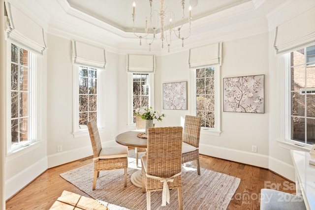 dining space with a tray ceiling, light wood finished floors, ornamental molding, a chandelier, and baseboards