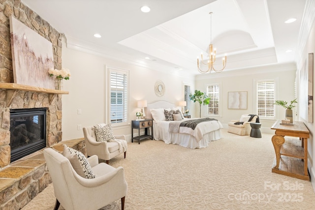 carpeted bedroom with ornamental molding, a chandelier, a tray ceiling, and a stone fireplace