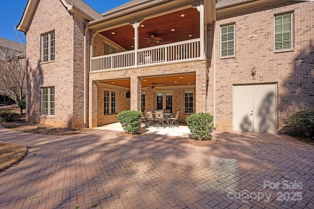 rear view of house with a balcony, a patio area, ceiling fan, and brick siding