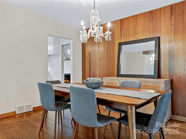 dining area featuring a fireplace, hardwood / wood-style floors, an inviting chandelier, and wooden walls