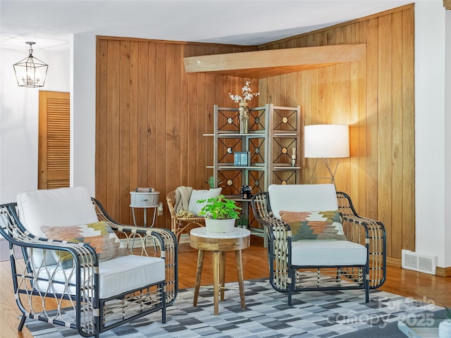 living area with hardwood / wood-style flooring, wooden walls, and an inviting chandelier