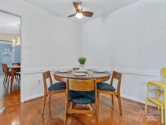 dining area featuring ceiling fan with notable chandelier and wood-type flooring