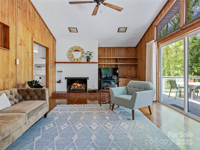 living room with a brick fireplace, wooden walls, a textured ceiling, and hardwood / wood-style flooring