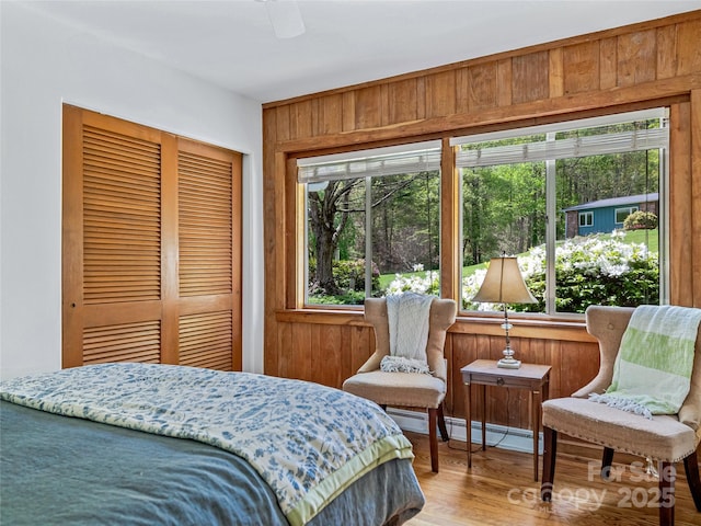 bedroom with wooden walls, a baseboard heating unit, ceiling fan, a closet, and wood-type flooring