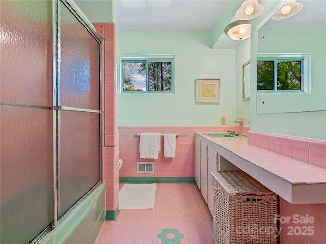 full bathroom with toilet, bath / shower combo with glass door, tile walls, vanity, and tile patterned floors