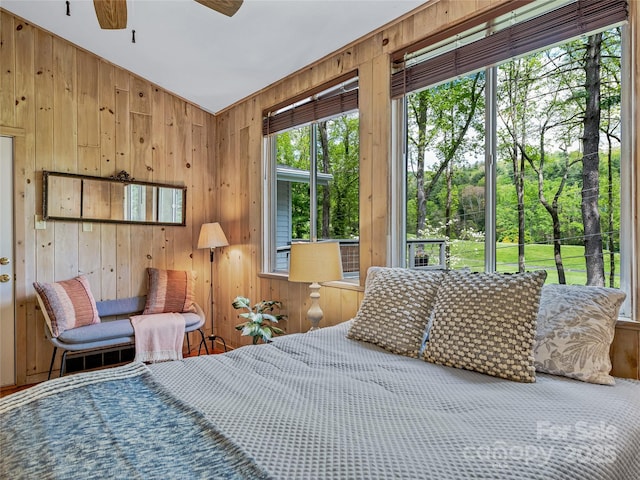 bedroom with ceiling fan, multiple windows, and wooden walls