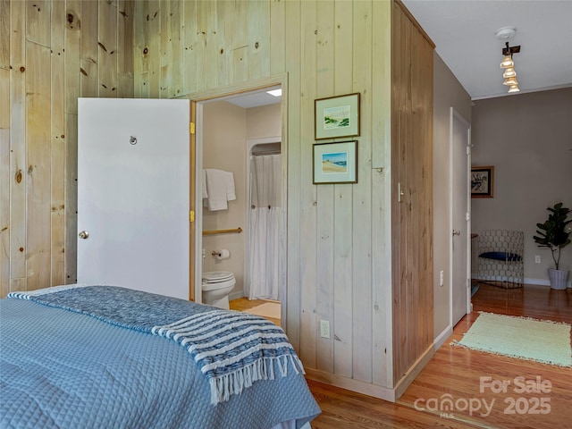 bedroom featuring ensuite bath, hardwood / wood-style floors, and wood walls