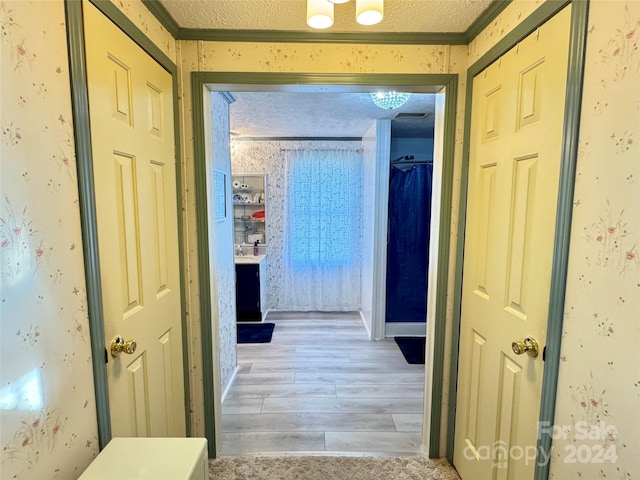 hallway featuring a textured ceiling, light wood-type flooring, and ornamental molding