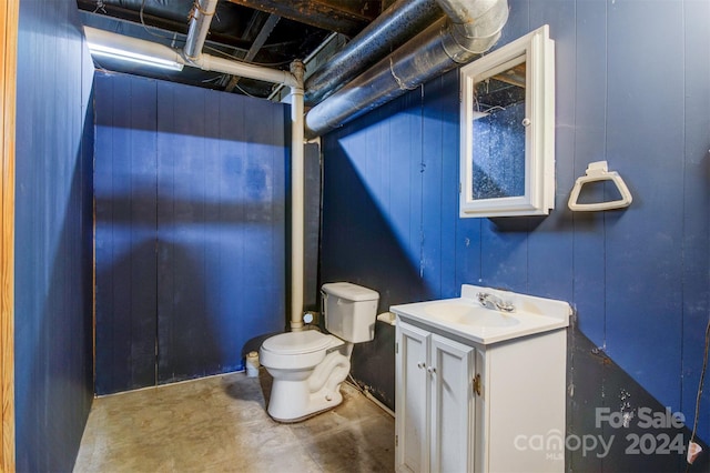 bathroom with wooden walls, vanity, concrete flooring, and toilet