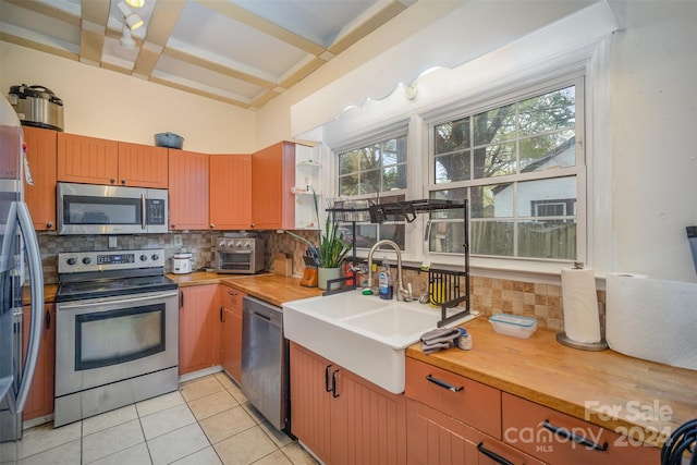 kitchen with sink, light tile patterned floors, tasteful backsplash, beam ceiling, and stainless steel appliances