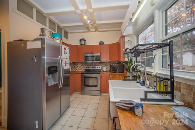 kitchen with sink, coffered ceiling, beamed ceiling, backsplash, and appliances with stainless steel finishes