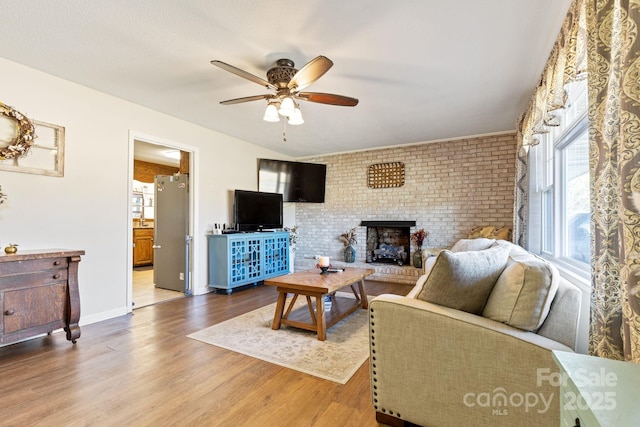 living room featuring a brick fireplace, hardwood / wood-style floors, ceiling fan, and brick wall