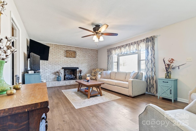 living room featuring hardwood / wood-style flooring, a brick fireplace, and ceiling fan