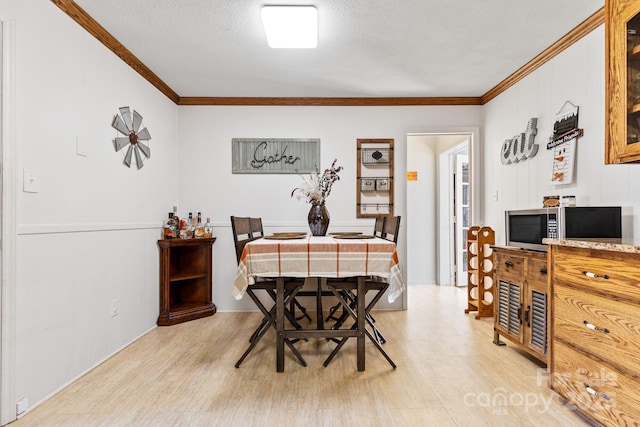 dining room with ornamental molding, light hardwood / wood-style floors, and a textured ceiling