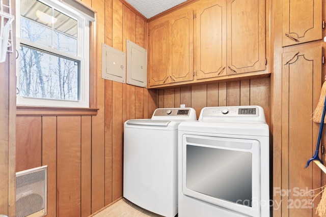 washroom featuring cabinets, a healthy amount of sunlight, washer and clothes dryer, and wood walls