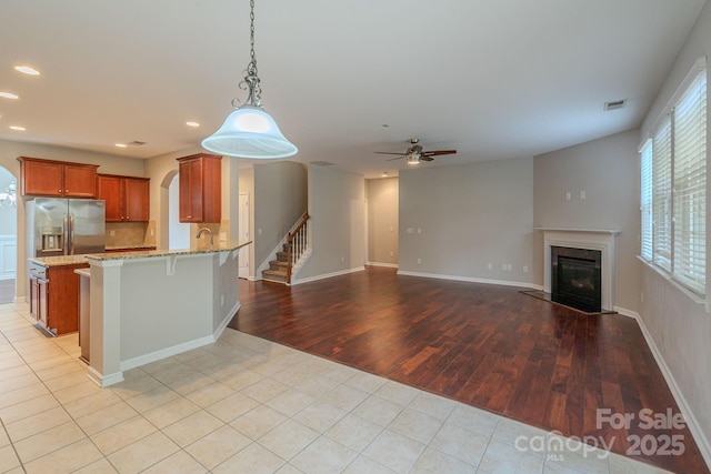 kitchen with stainless steel fridge, visible vents, brown cabinetry, a glass covered fireplace, and a peninsula