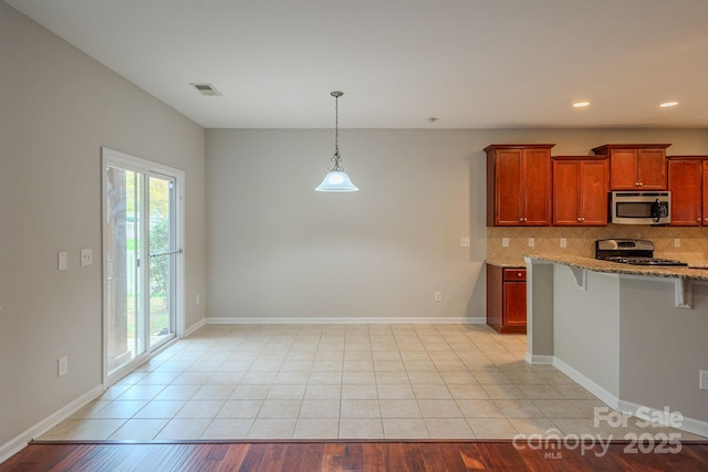 kitchen with baseboards, decorative backsplash, a breakfast bar, light stone countertops, and stainless steel appliances