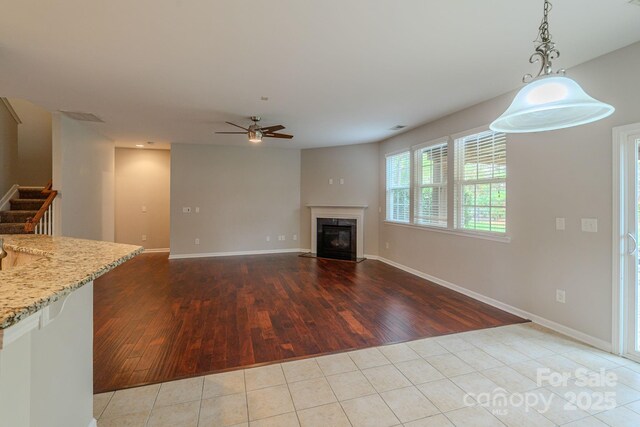 unfurnished living room featuring stairway, a premium fireplace, ceiling fan, wood finished floors, and baseboards