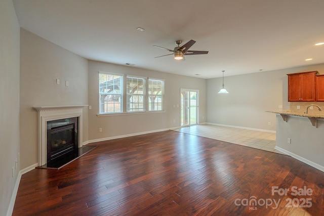 unfurnished living room featuring a healthy amount of sunlight, baseboards, wood finished floors, and a glass covered fireplace