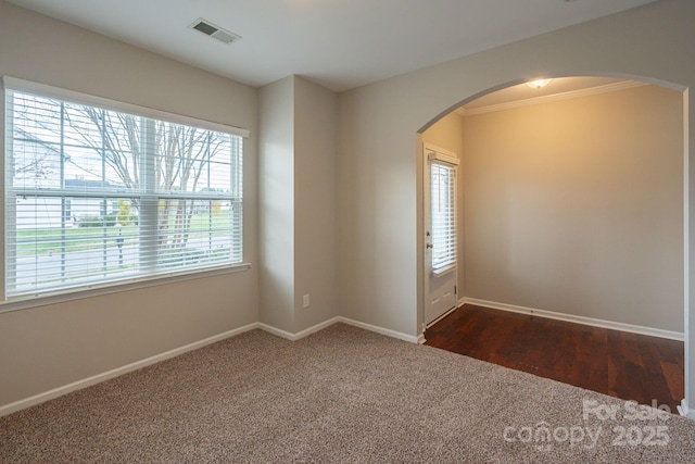 spare room featuring baseboards, visible vents, arched walkways, ornamental molding, and dark carpet