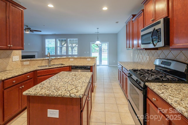 kitchen with light tile patterned floors, stainless steel appliances, a sink, light stone countertops, and a peninsula