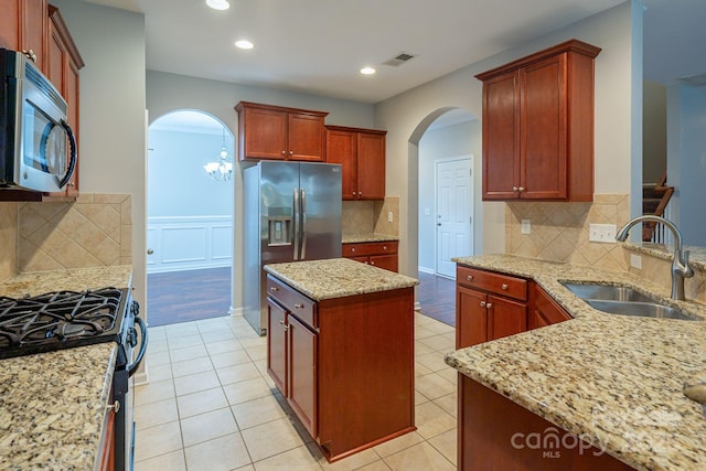 kitchen with visible vents, a kitchen island, appliances with stainless steel finishes, light stone counters, and a sink