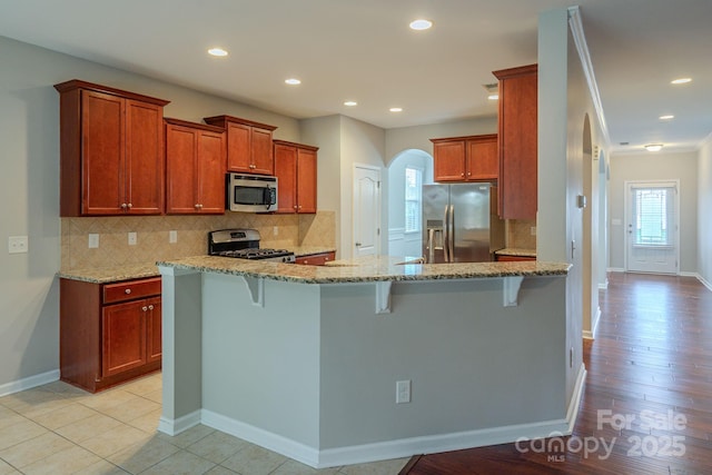 kitchen with light stone counters, arched walkways, stainless steel appliances, and a breakfast bar area