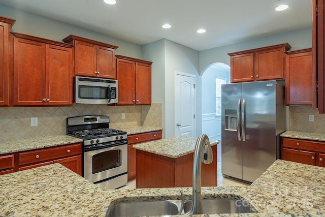 kitchen featuring arched walkways, a sink, appliances with stainless steel finishes, backsplash, and light stone countertops