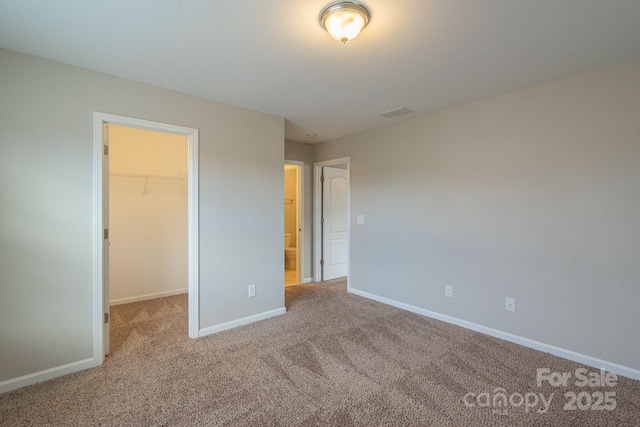 unfurnished bedroom with a closet, carpet, a walk in closet, and baseboards