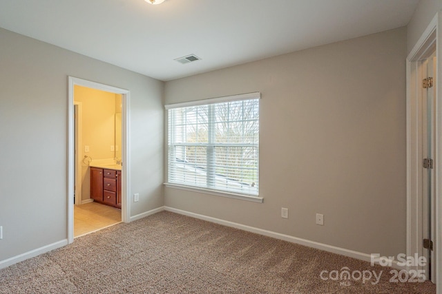 unfurnished bedroom featuring light carpet, ensuite bath, visible vents, and baseboards