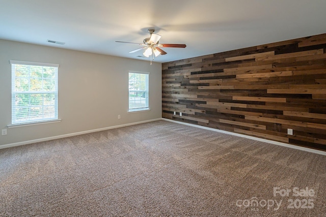 empty room featuring carpet, visible vents, wooden walls, and baseboards