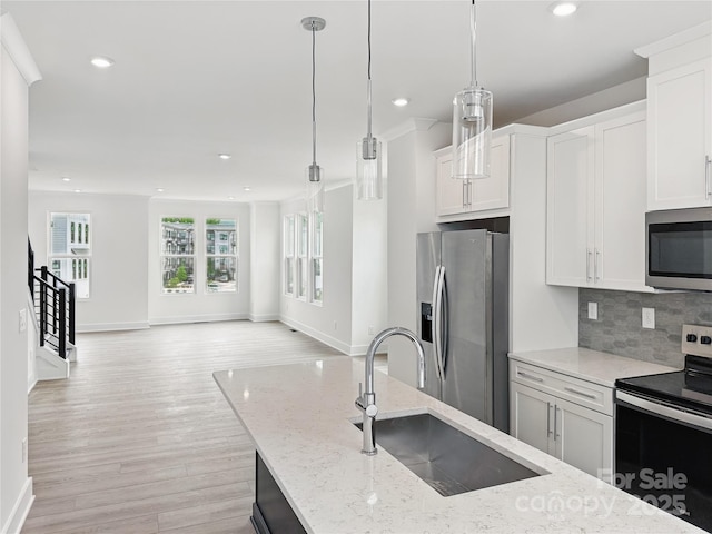 kitchen with a sink, tasteful backsplash, light wood-style flooring, appliances with stainless steel finishes, and open floor plan