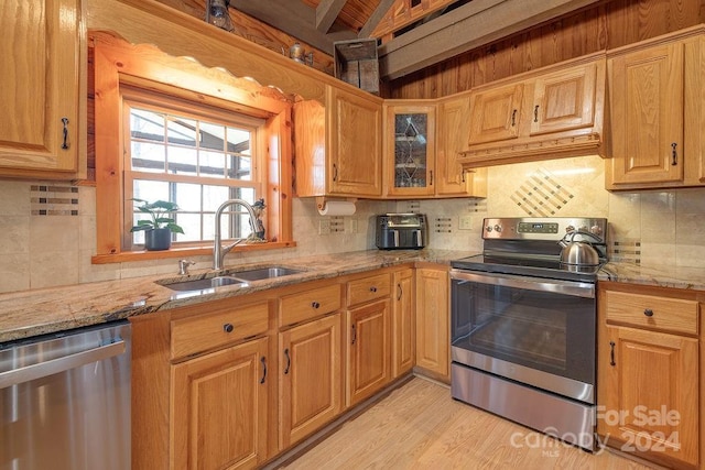 kitchen featuring backsplash, sink, light stone countertops, light wood-type flooring, and stainless steel appliances