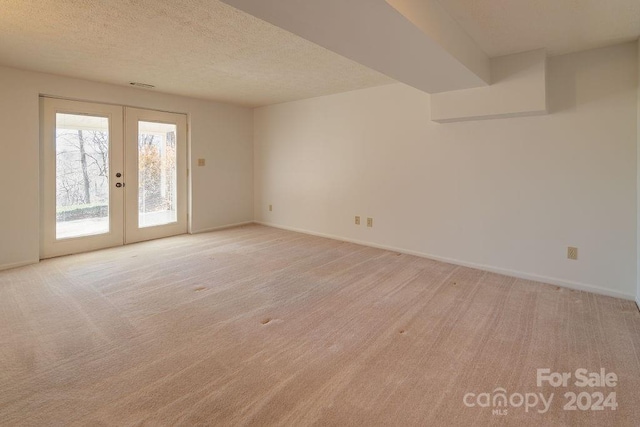 empty room with french doors, a textured ceiling, and light colored carpet