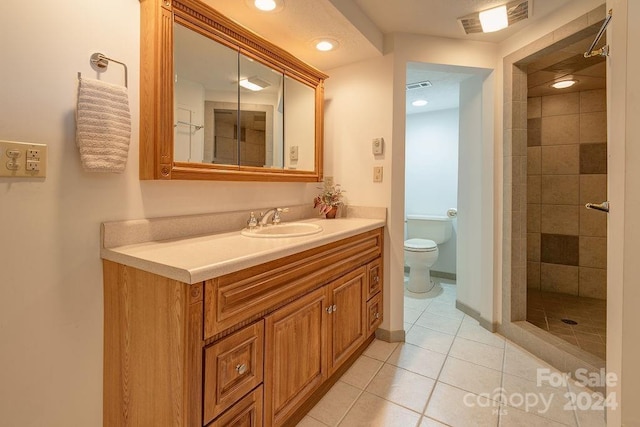 bathroom with tile patterned floors, vanity, toilet, and a tile shower