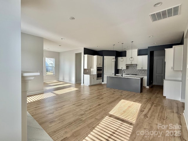 405 Northgate Blvd, Indian Trail, NC 28079 - kitchen featuring open floor plan, a kitchen island with sink, backsplash, light wood-style floors, and white cabinets