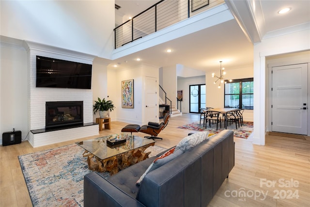 living room with crown molding, a towering ceiling, a chandelier, light hardwood / wood-style floors, and a fireplace