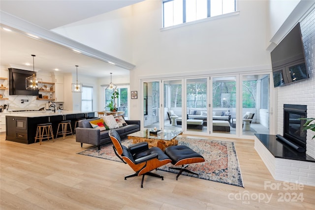 living room featuring sink, a towering ceiling, light hardwood / wood-style floors, and a brick fireplace