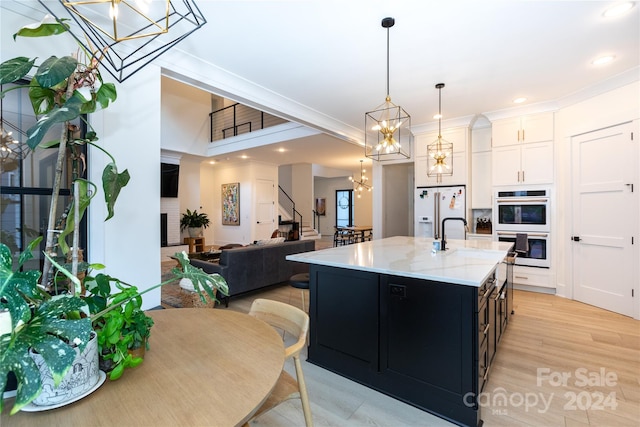 kitchen featuring pendant lighting, white appliances, a kitchen island with sink, white cabinets, and light hardwood / wood-style flooring