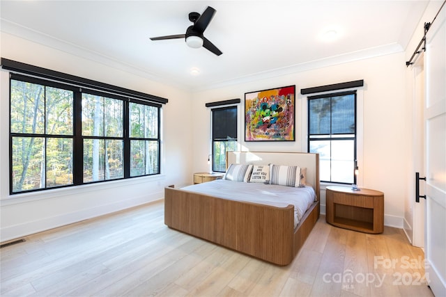 bedroom with a barn door, light hardwood / wood-style flooring, ceiling fan, and ornamental molding