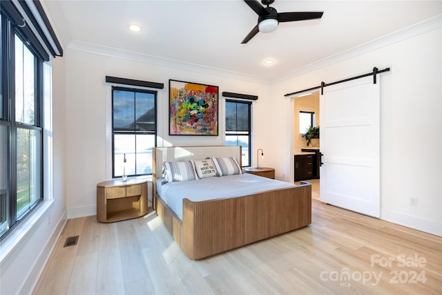 bedroom featuring a barn door, light hardwood / wood-style floors, multiple windows, and ceiling fan