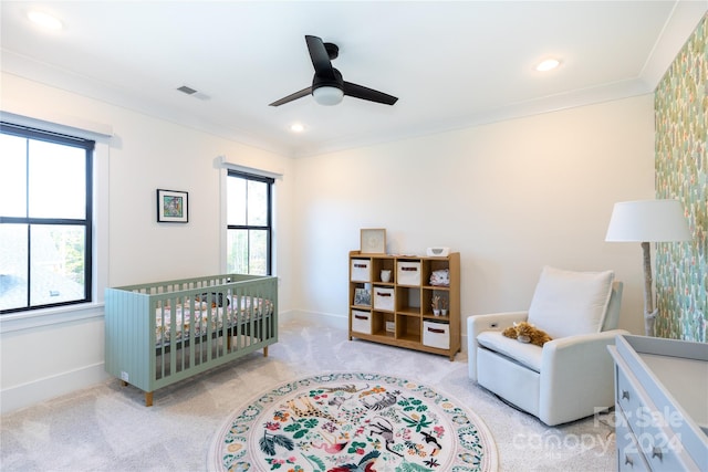 bedroom featuring ceiling fan, light colored carpet, a crib, and ornamental molding